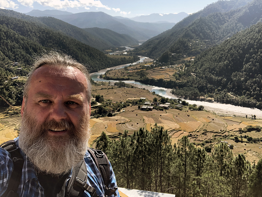 Zdjęcie przedstawia uśmiechniętego autora bloga, za nim widać dolinę Punakhy w Bhutanie