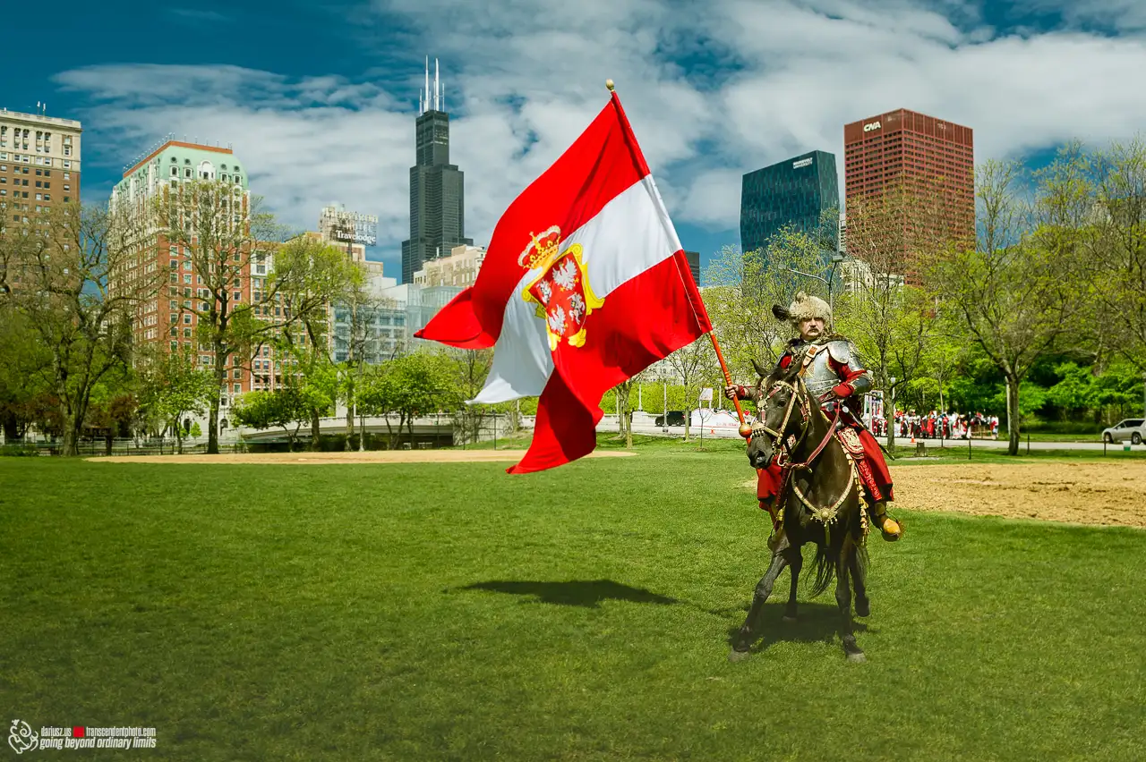 Rekonstruktor w zbroi polskiego husarza na koniu, trzymający flagę Polski z godłem, na tle wieżowców w centrum Downtown Chicago.
