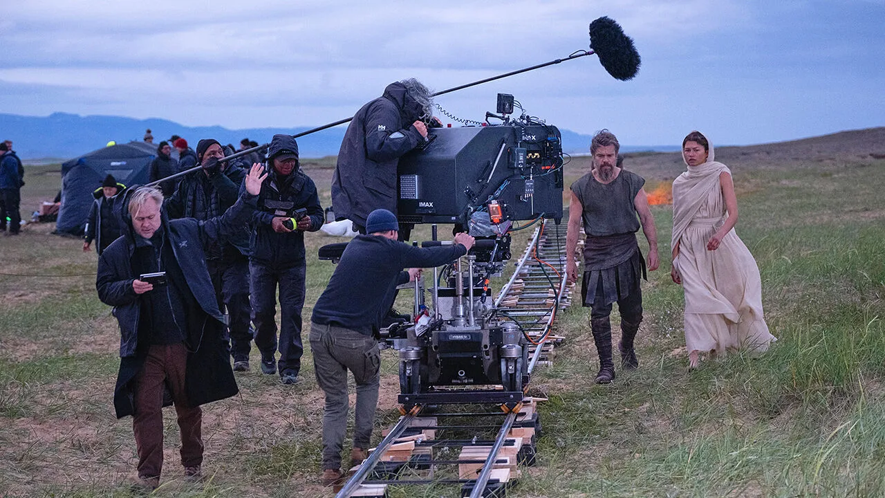 Movie set with large camera, crew, and costumed actors outdoors.