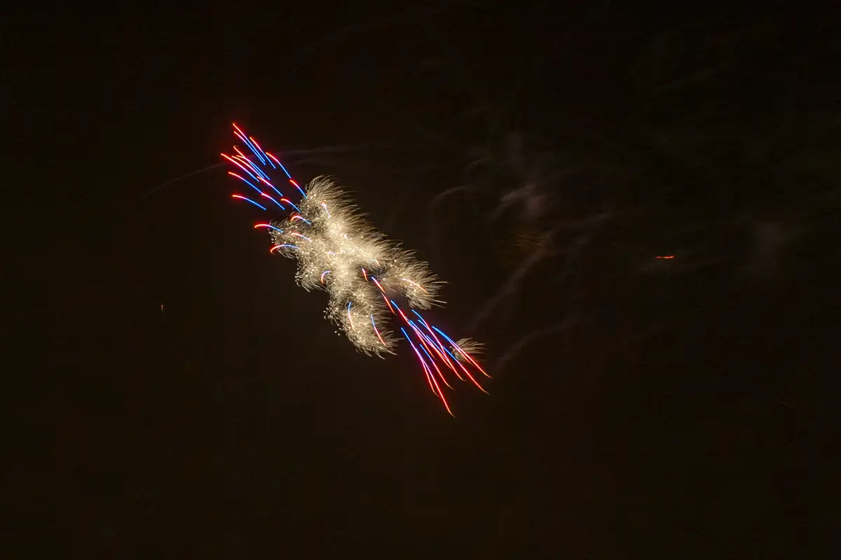Bright white fireworks burst with red and blue trails in night sky.