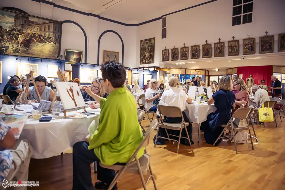 Adults painting in a large room surrounded by artworks.