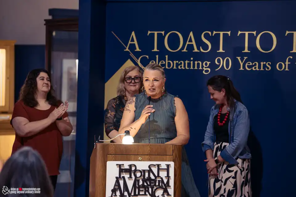 Woman speaking at podium, others applauding at museum event.