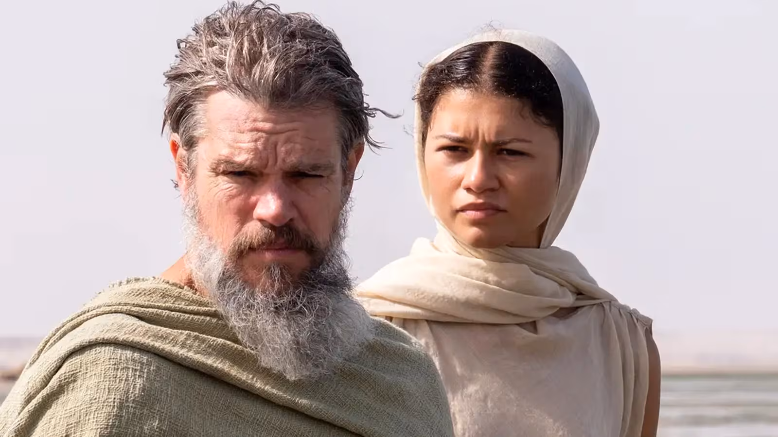 Man with beard and woman in head covering in arid landscape.