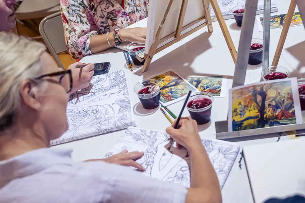 People coloring designs at a table with drinks and easels.