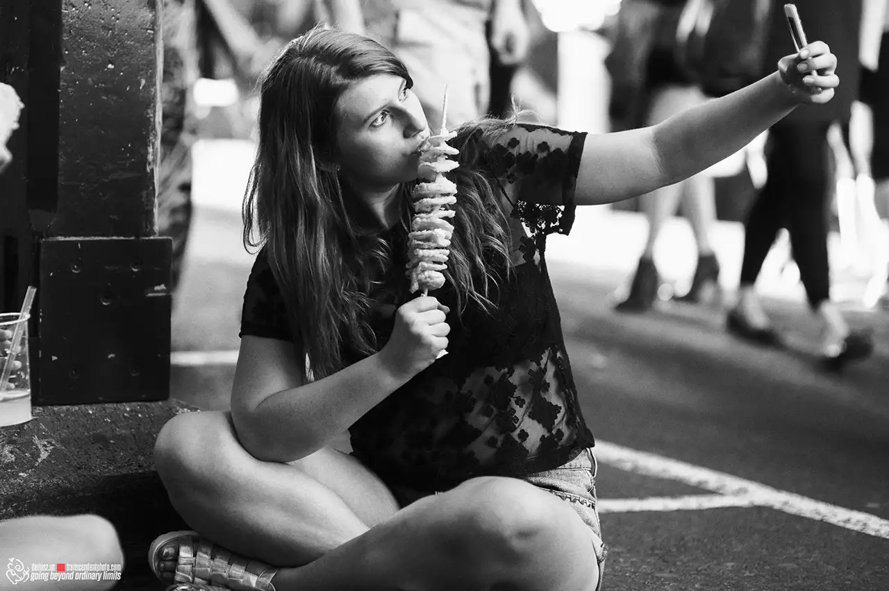 Woman eating spiral fries, taking selfie in black and white.
