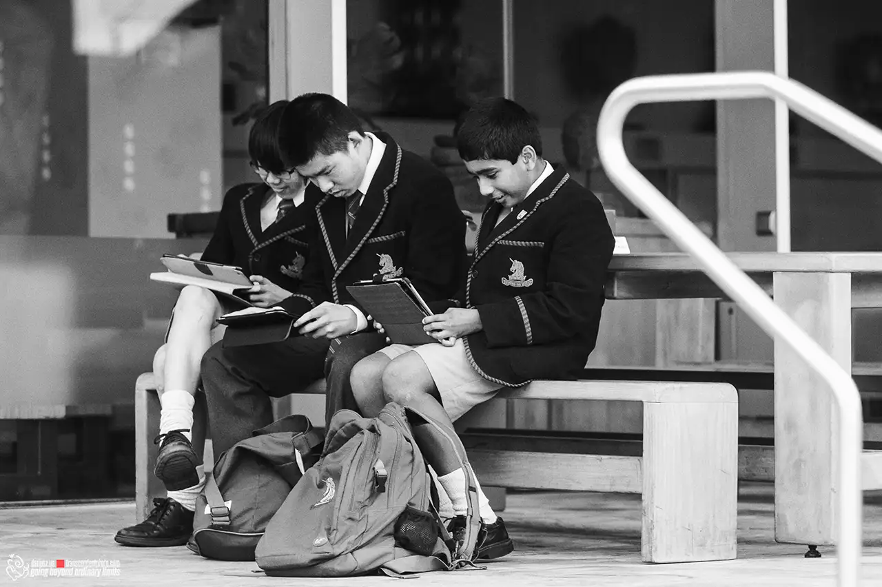 Three uniformed students on a bench using tablets.