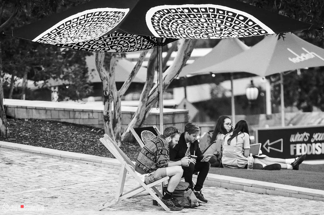 People relaxing outdoors under decorative umbrellas in black and white.