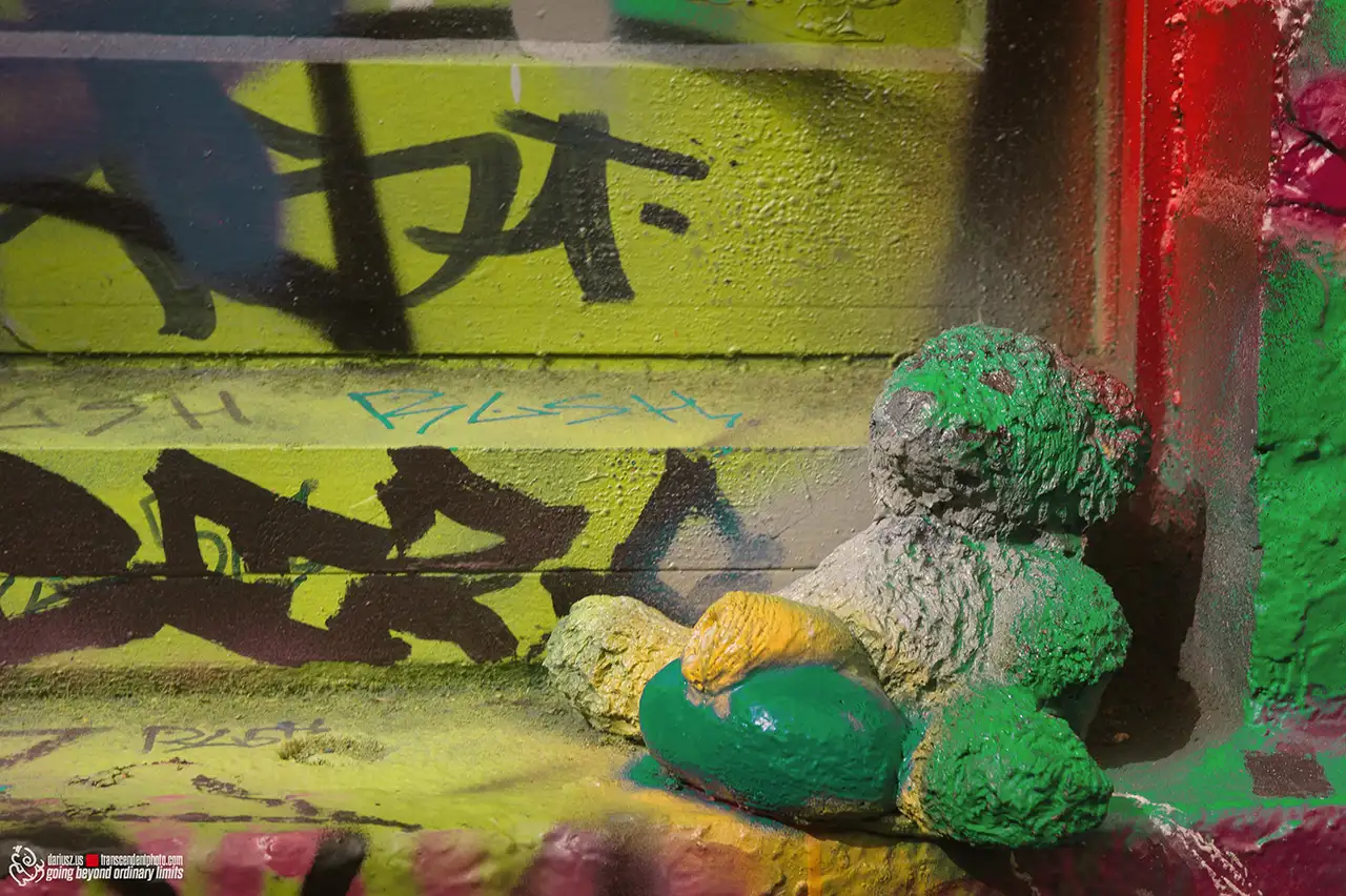 Paint-covered teddy bear against vibrant graffiti wall.