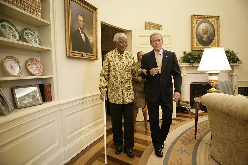 Nelson Mandela and George W. Bush walk arm-in-arm in a room.