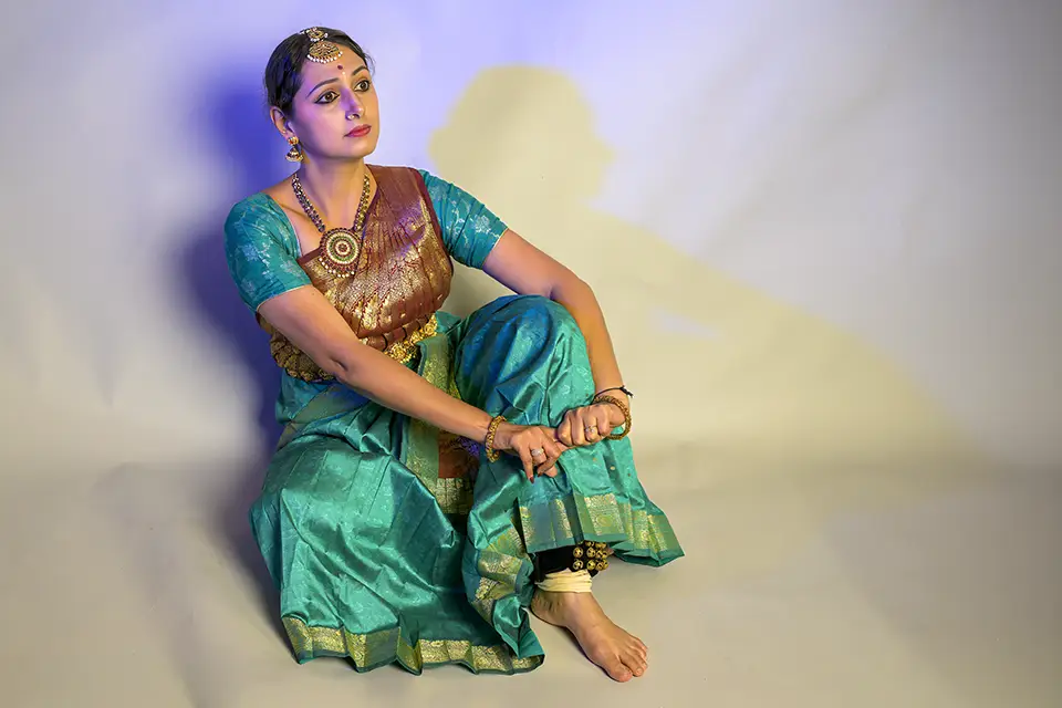 Indian classical dancer in traditional teal saree and gold jewelry.