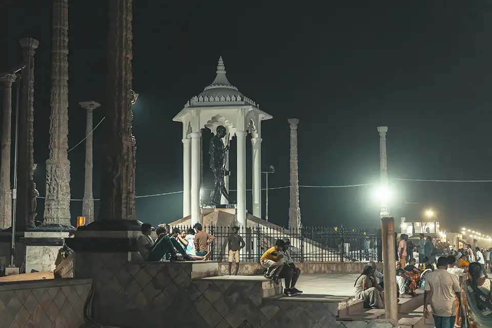 Mahatma Gandhi statue at night, surrounded by carved pillars.