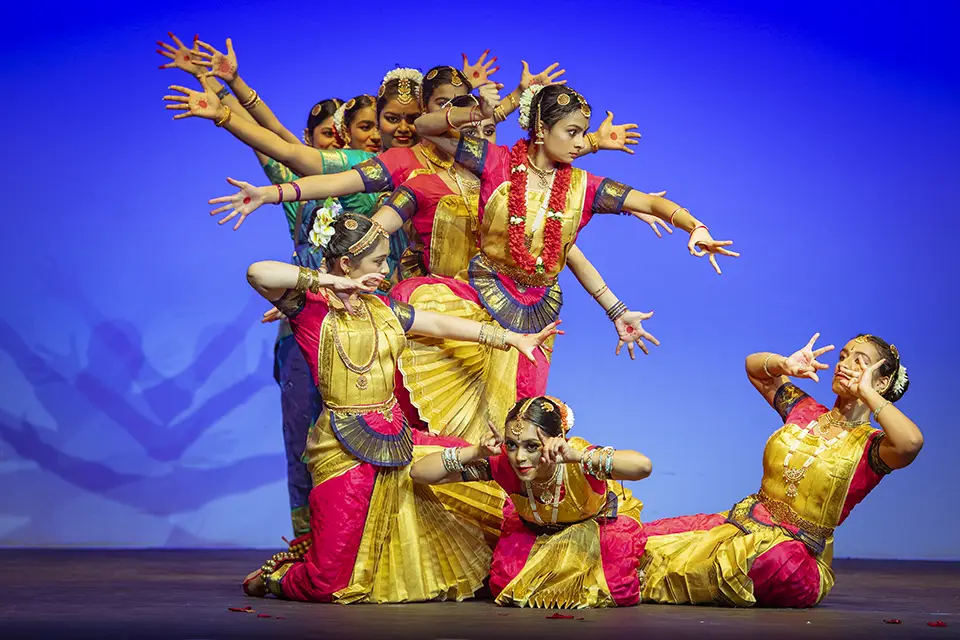 Indian classical dancers in vibrant costumes performing on stage.
