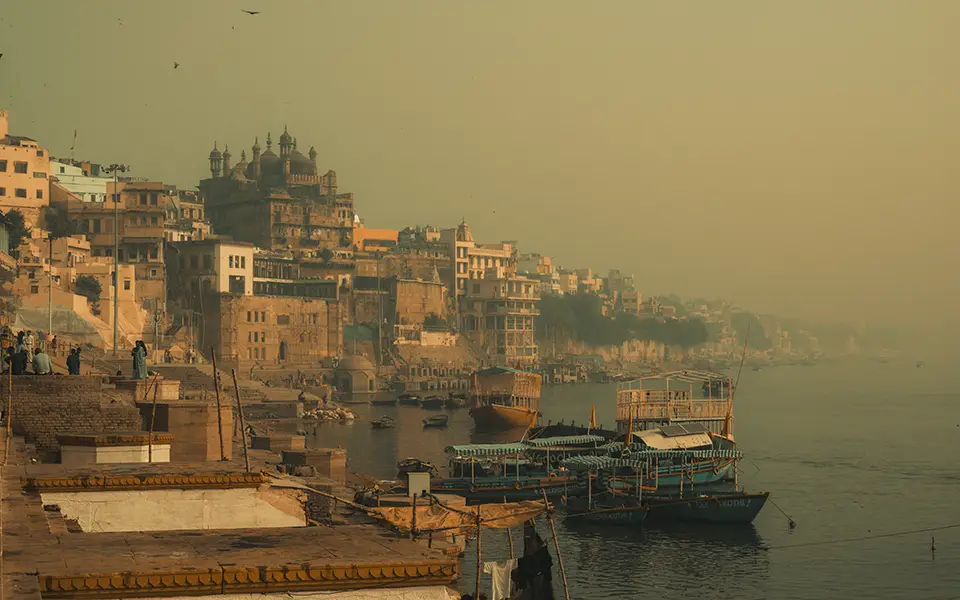Misty morning view of historic city ghats and boats on Ganges river.