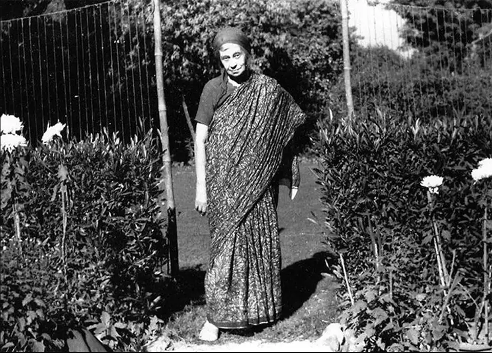 Woman in sari and head covering stands in a garden.