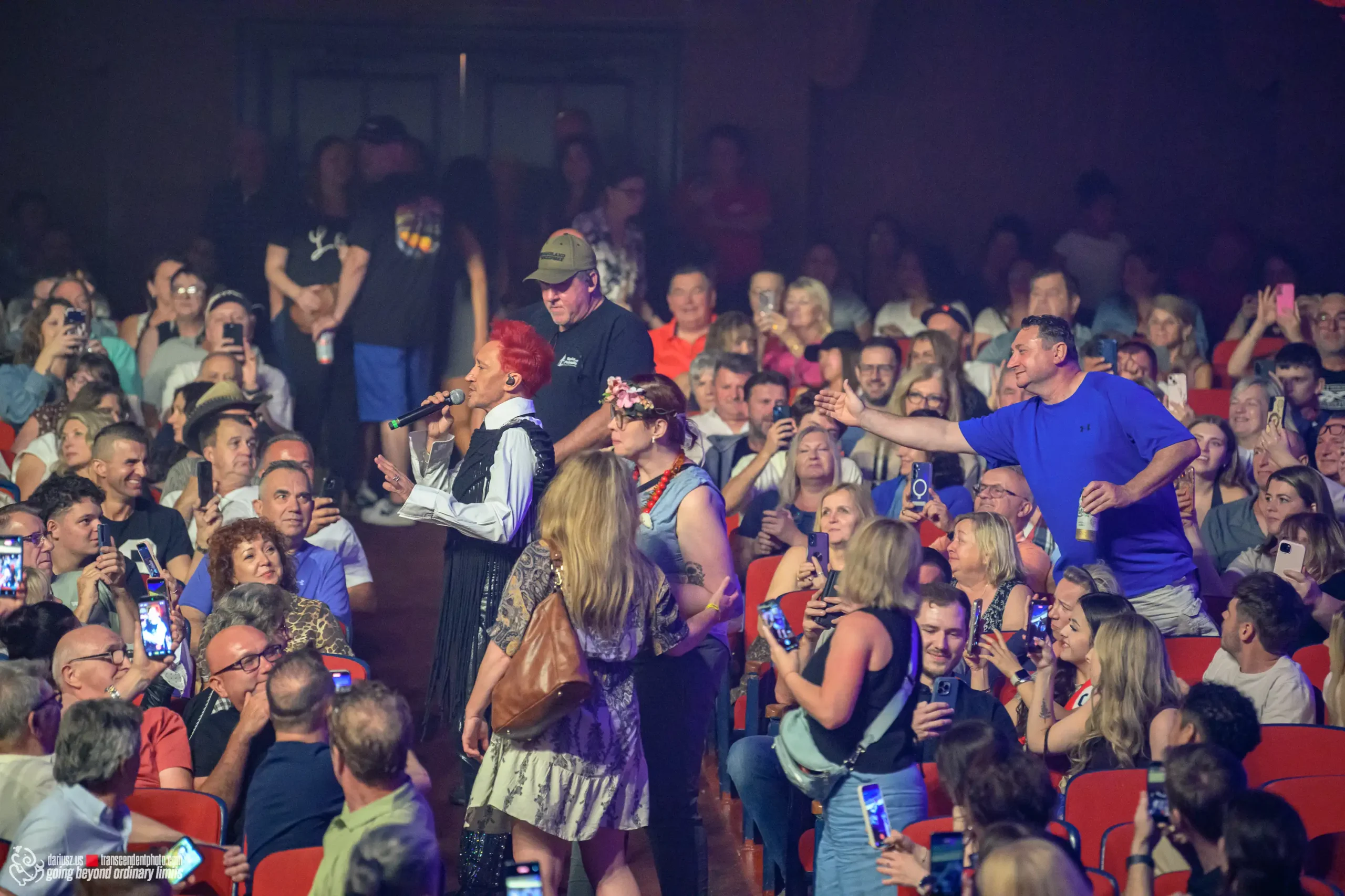 Michał Wiśniewski with red hair on stage, audience filming with phones.