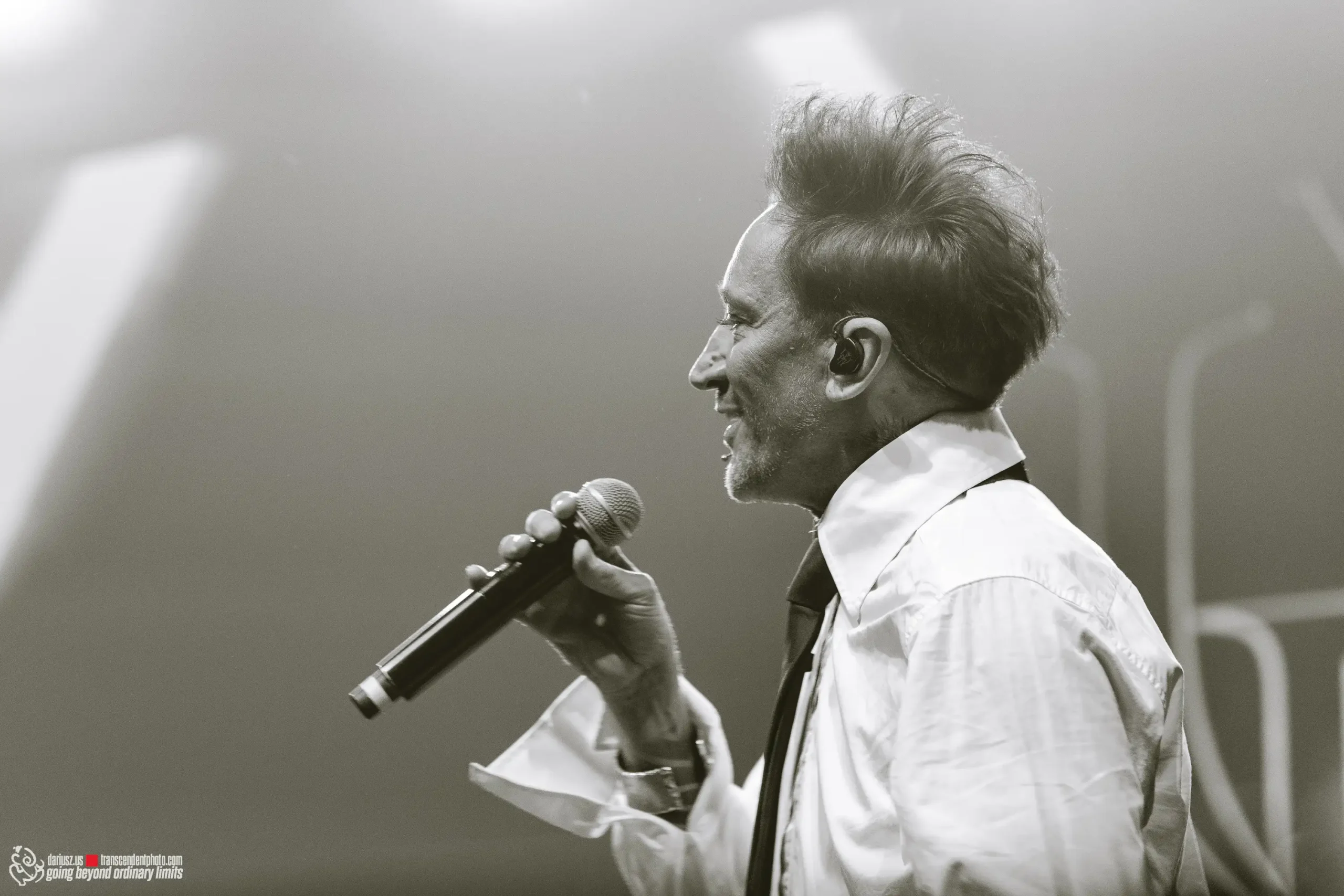 Smiling male singer in profile holding microphone onstage.