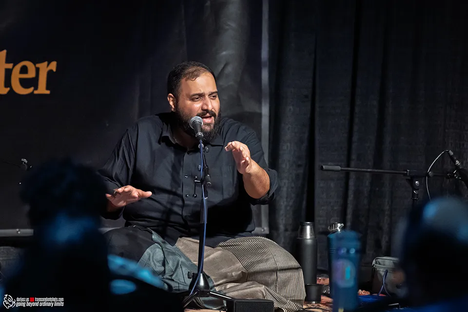 Man speaking into microphone on stage with expressive hands.