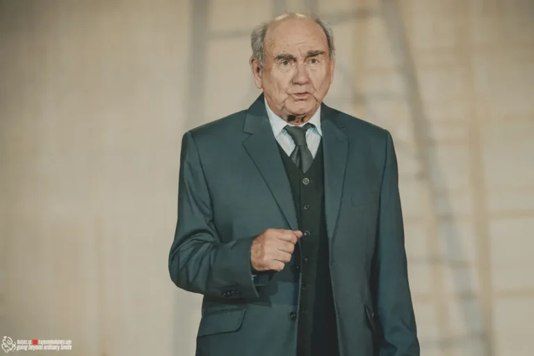Older man in dark suit and tie, looking forward.