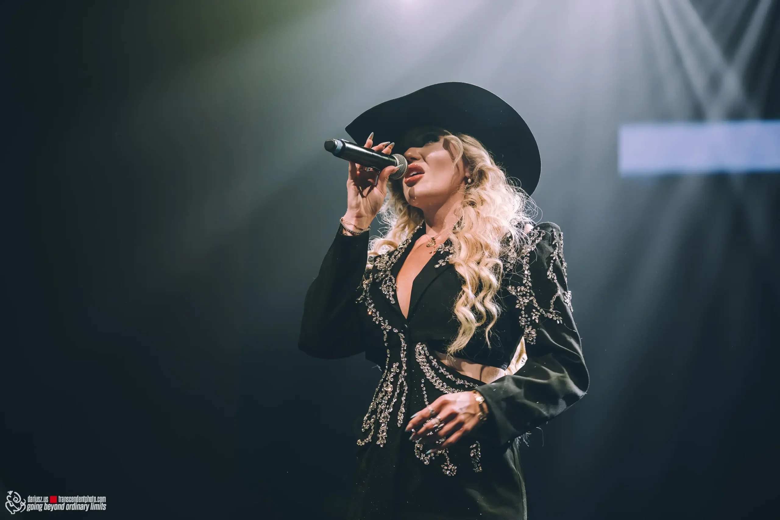 Woman singing on stage in hat and embellished black jacket.