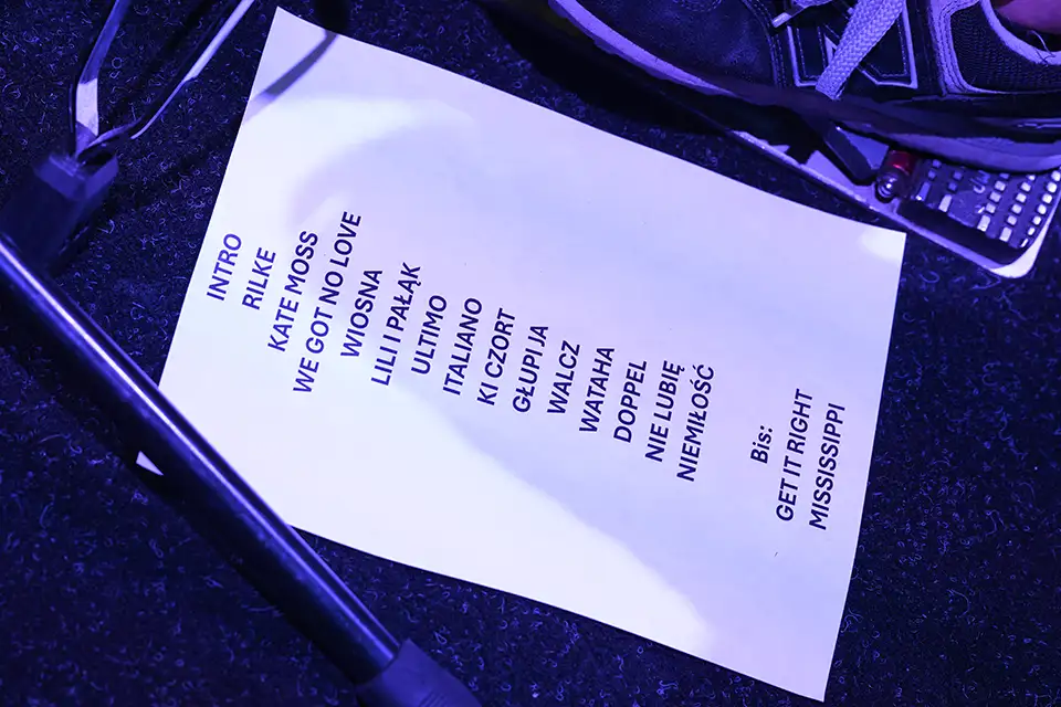 Concert setlist with song titles on stage under purple light.