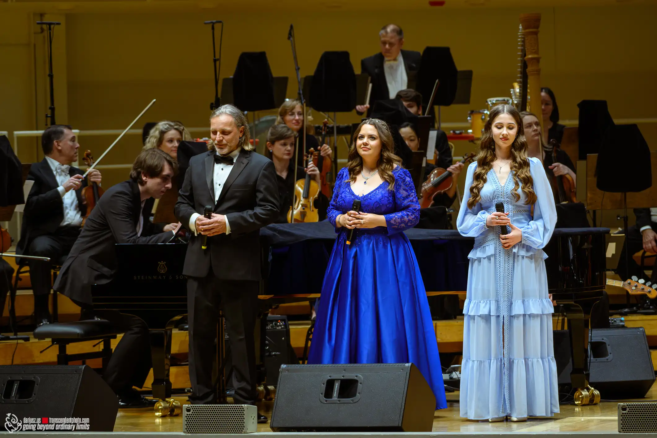Three vocalists and an orchestra perform on a concert stage.