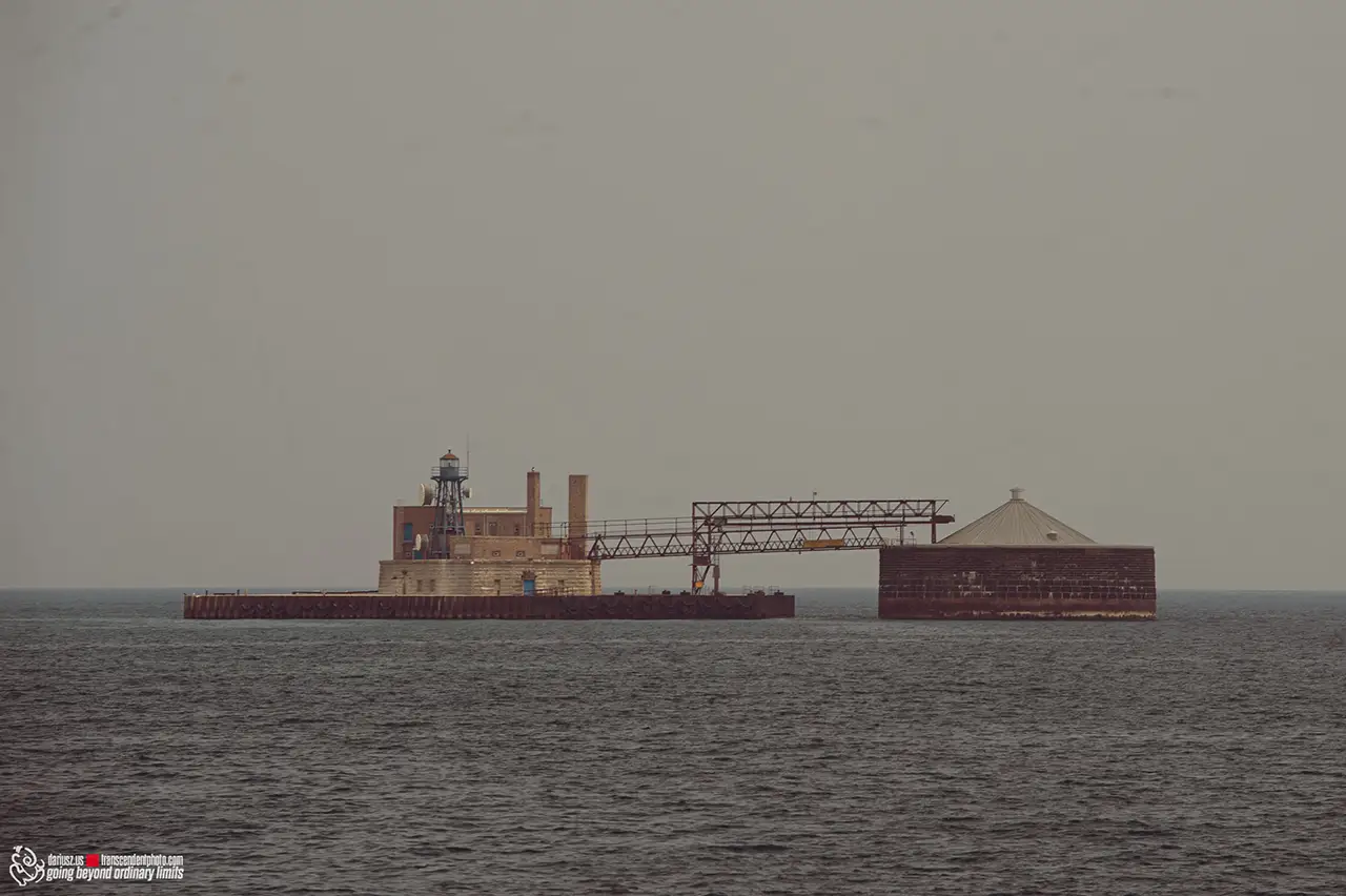 Industrial complex with lighthouse and silo on water.