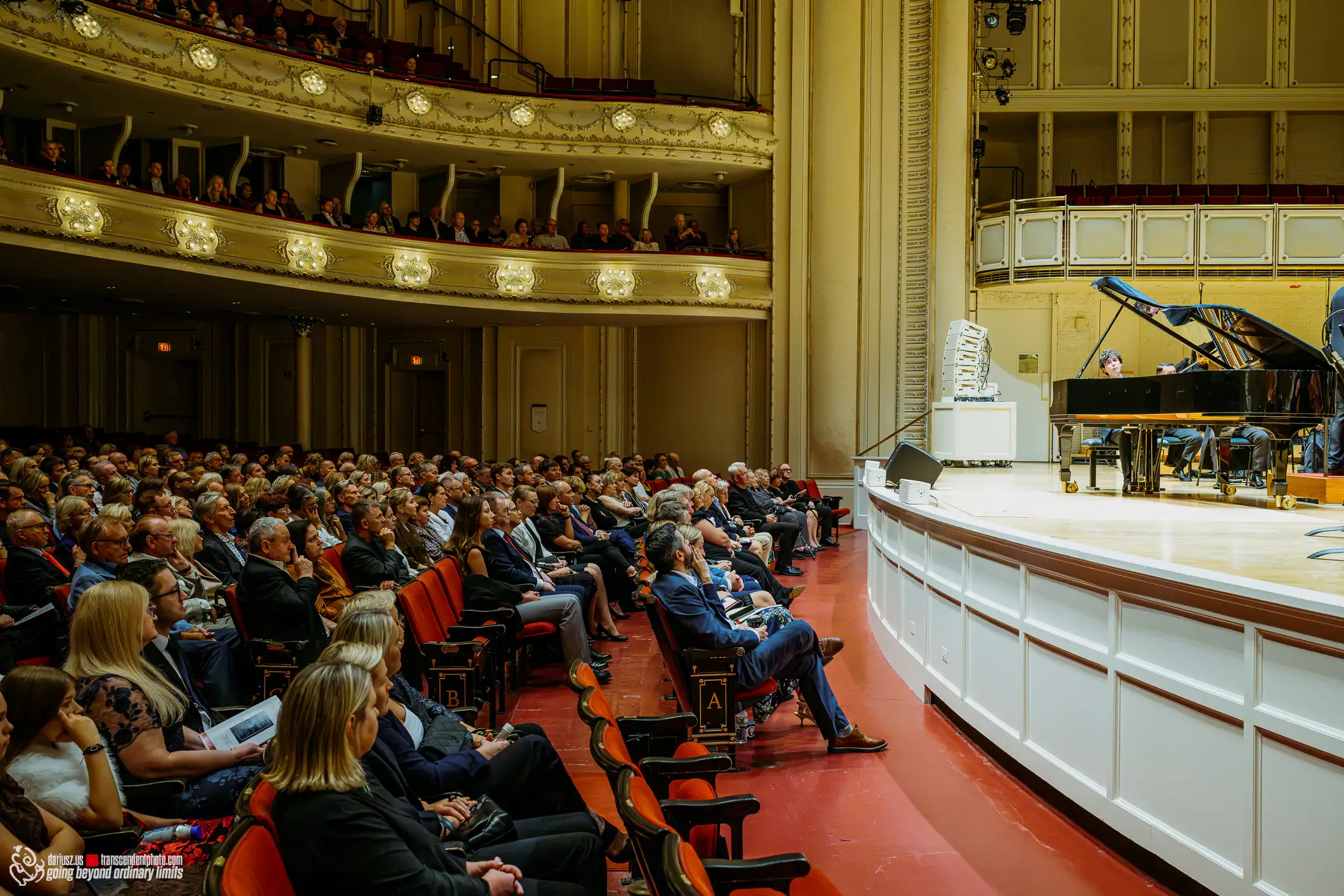 Audience watches pianist on stage in grand concert hall.