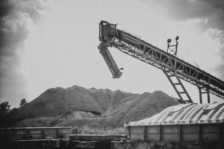 Black and white photo of industrial conveyor, material piles, and barges.